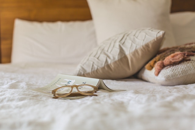 Vista de unas sábanas con almohadas con unas gafas y un libro encima
